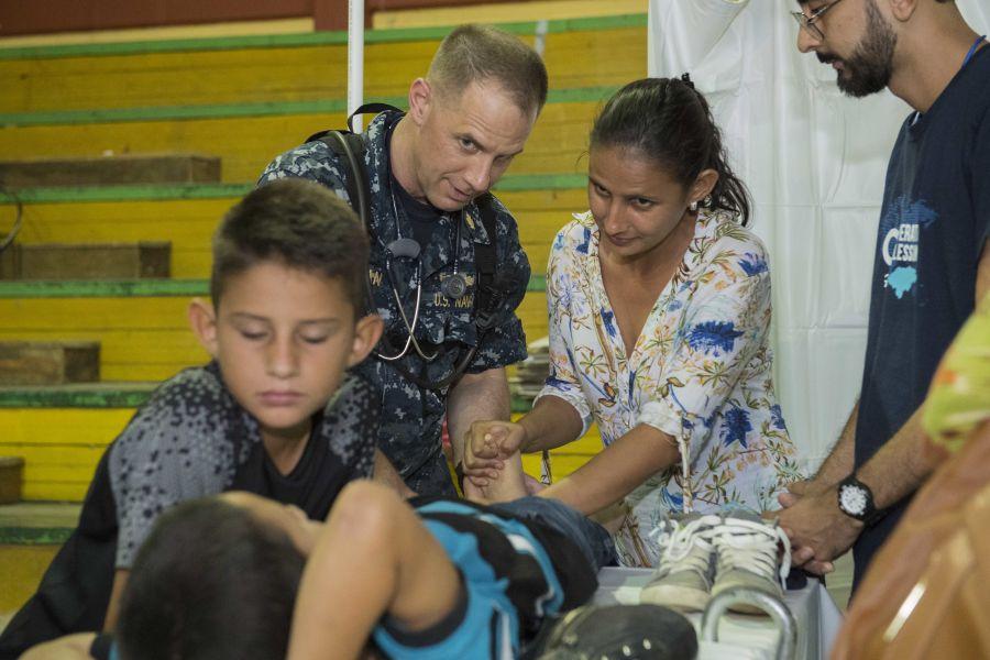 U.S. Navy Captain Matthew McLean, assigned to the Naval Medical Center in Portsmouth, Massachusetts, shows the mother of a child who has a lesion on his Achilles tendon how to do physical therapy at the Franklin D. Roosevelt School in Puerto Cortés, Honduras, on March 15th. (Photo: U.S. Navy Specialist Second Class Brianna K. Green)