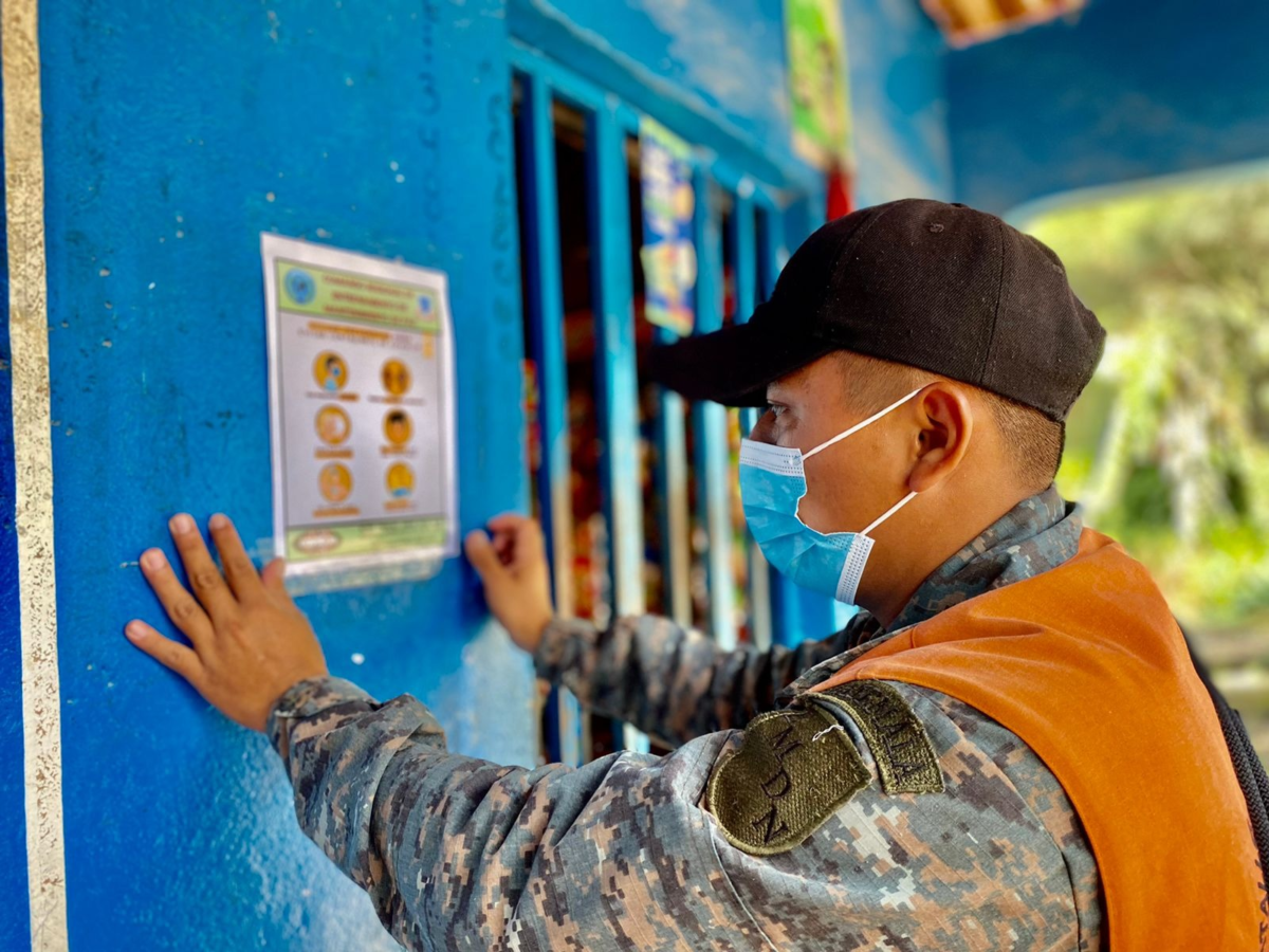 A Guatemalan soldier tapes a document on the wall of a local store, near the city of Cobán, with instructions for people on how to protect themselves against COVID-19. (Photo: Guatemalan Army)