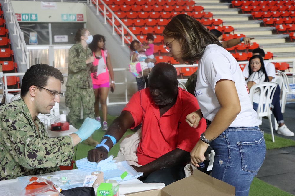 U.S. Navy Hospital Corpsman Third Class Dominic Baucco (L), assigned to hospital ship USNS Comfort, draws a blood sample for testing, while Claudia German, a volunteer with Dominican organization Sanar Una Nación, translates for the patient at a medical site in Santo Domingo, Dominican Republic, November 29, 2022. (Photo: Geraldine Cook/Diálogo)