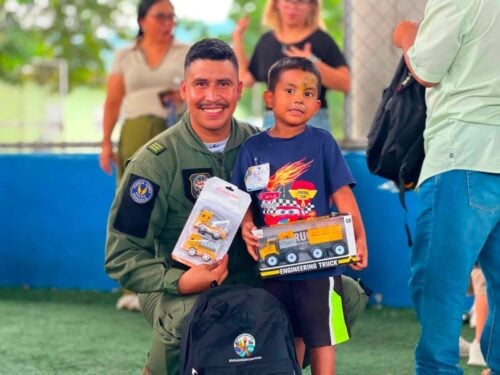 A Honduran military cadet kneels beside a young boy while presenting toys during a day of games and activities organized by the Honduran Military Aviation Academy with support from Joint Task Force-Bravo.