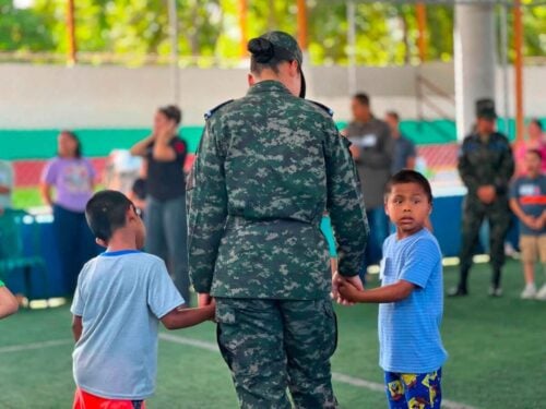 A Honduran military cadet walks hand in hand with two children during recreational activities at Nazareth Orphanage, where volunteers spent the day engaging with the children through games and fellowship.