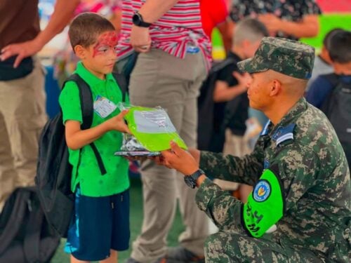 A Honduran military cadet presents a gift to a child during a community outreach event that included the distribution of toys, food, and other donated items.