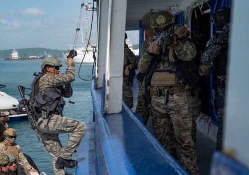 Panamanian security forces, with the support of U.S. Southern Command (SOUTHCOM), conducted Phase I of PANAMAX Alpha 2025, in late July – early August. The Panama Canal security exercise included simulated overhead support; visit, board, search, and seizure operations; fast rope insertions; aerial overwatch training, and much more. The following images offer a glimpse into the exercise.
A Panamanian National Border Service (SENAFRONT) member boards a vessel, while another provides cover during a bilateral simulated visit, board, search, and seizure training between U.S. and Panamanian special forces units as part of PANAMAX Alpha Phase I, Panama City, Panama, July 17, 2025. (Photo: U.S. Air Force Staff Sergeant Sadie Colbert)